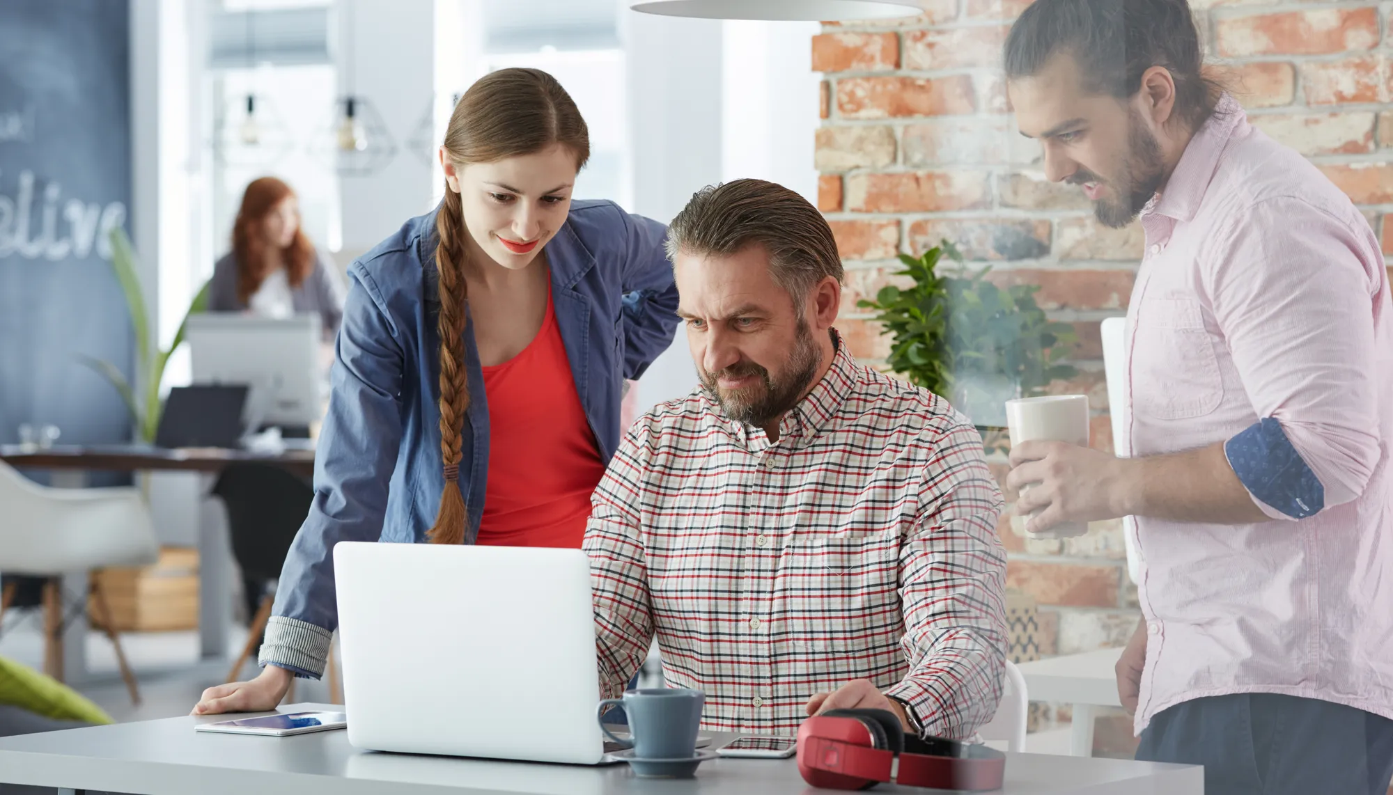 Älterer Firmenchef und junge Mitarbeiter arbeiten am Laptop