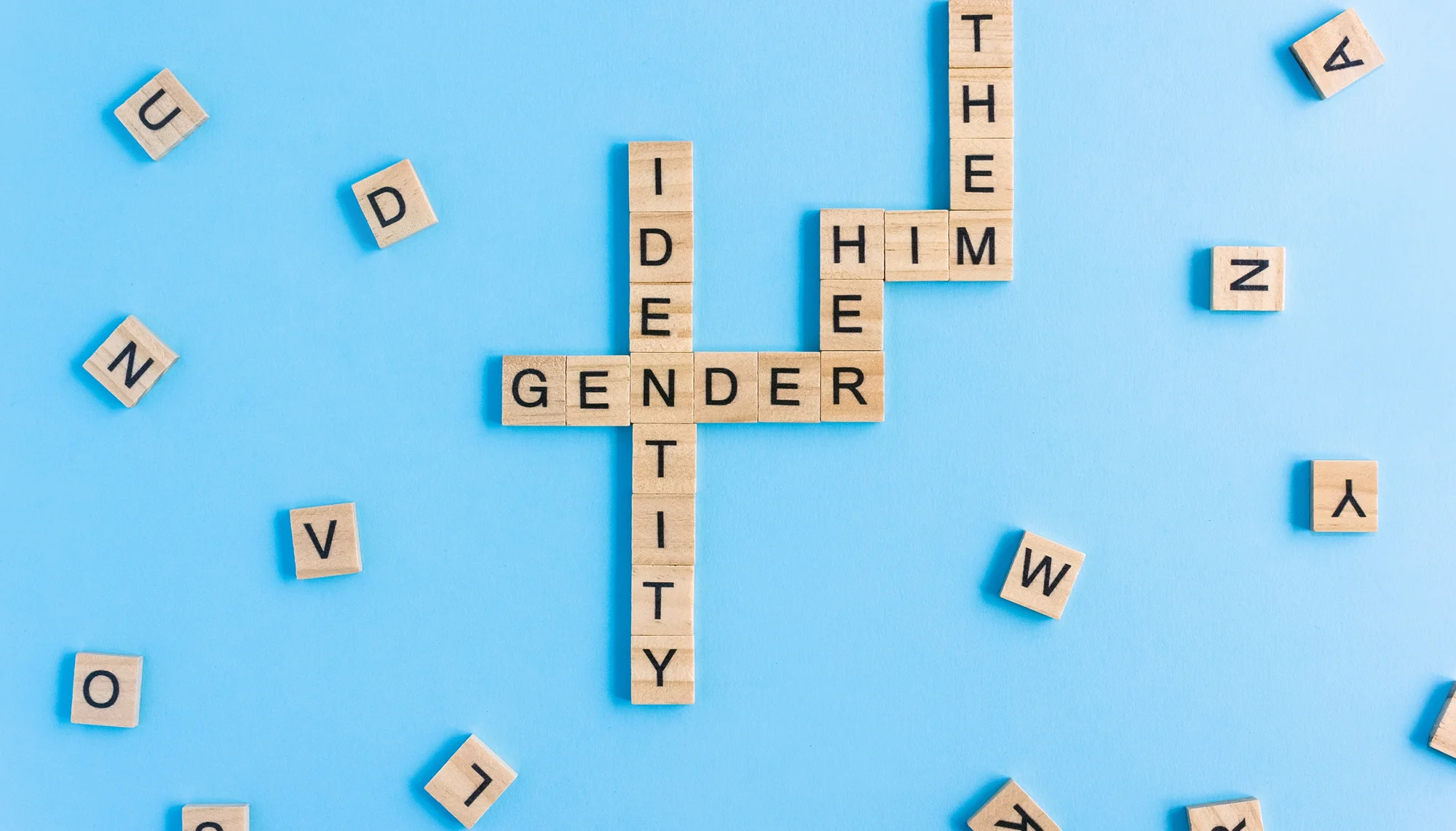 Scrabble-Spiel, Buchstabenreihen bilden die Wörter Identity, Gender, Her, Him, Them, lose Buchstabensteine liegen verteilt herum