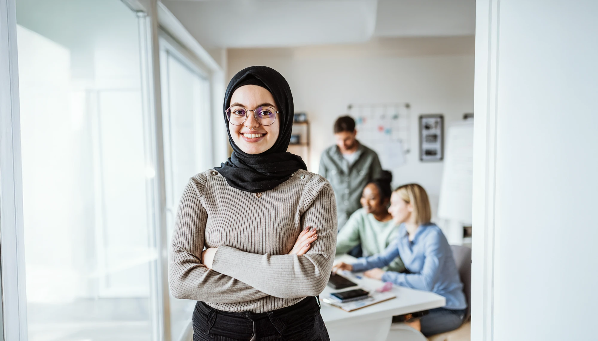 Muslima steht im Büro vor diversen Mitarbeiten:innen